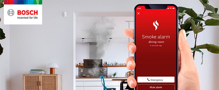 Bosch Smart Home app toont rookmelder-melding uit eetkamer met noodoproep-knop en rook uit keuken op achtergrond