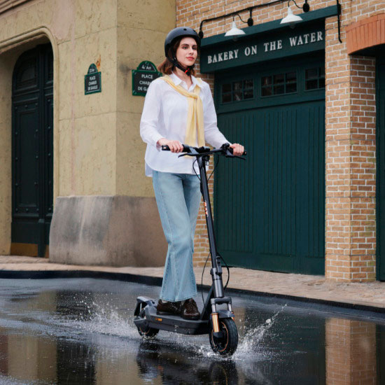Vrouw met helm rijdt op Navee GT elektrische step door plas op kasseien – spatwaterdicht en geschikt voor de stad