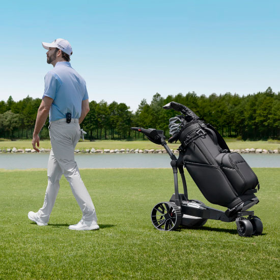 Golfer loopt naast de Navee elektrische golftrolley met golftas op de golfbaan
