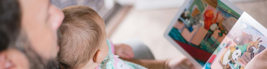 Vader met baby op schoot leest voor, cadeau-idee dat de aanwezigheid en tijd samen voor kersverse vaders versterkt.