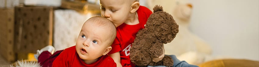 Broertje en zusje in rode kleding met knuffel, cadeau-idee voor grote zus of grote broer.