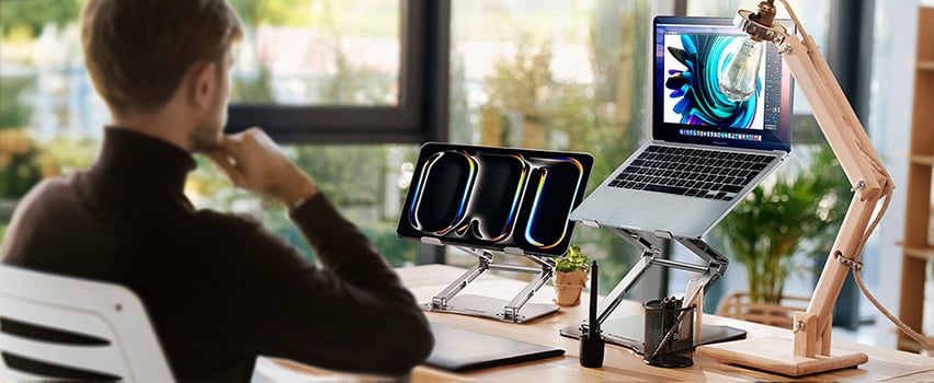 Man werkt aan bureau met laptop en tablet op Wozinsky verstelbare standaard in licht kantoor bij het raam
