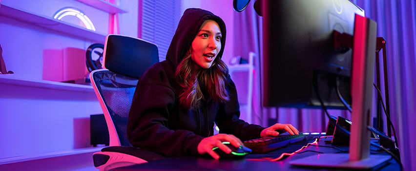Jonge vrouw gamet aan computer met Wozinsky gaming-muis en toetsenbord in donkere kamer met paarse RGB-verlichting