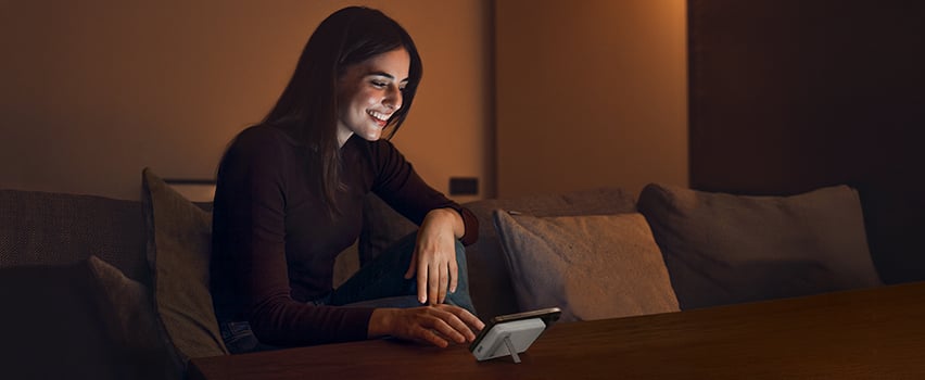 Vrouw glimlacht terwijl ze haar smartphone draadloos oplaadt met Wozinsky powerbank op tafel in gezellig avondlicht
