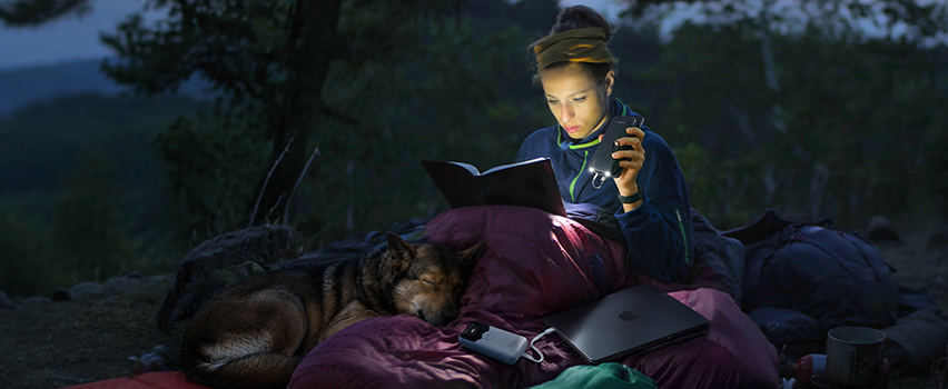 Vrouw leest boek in tent met hond en laadt smartphone en laptop op met Wozinsky powerbank en hoofdlamp